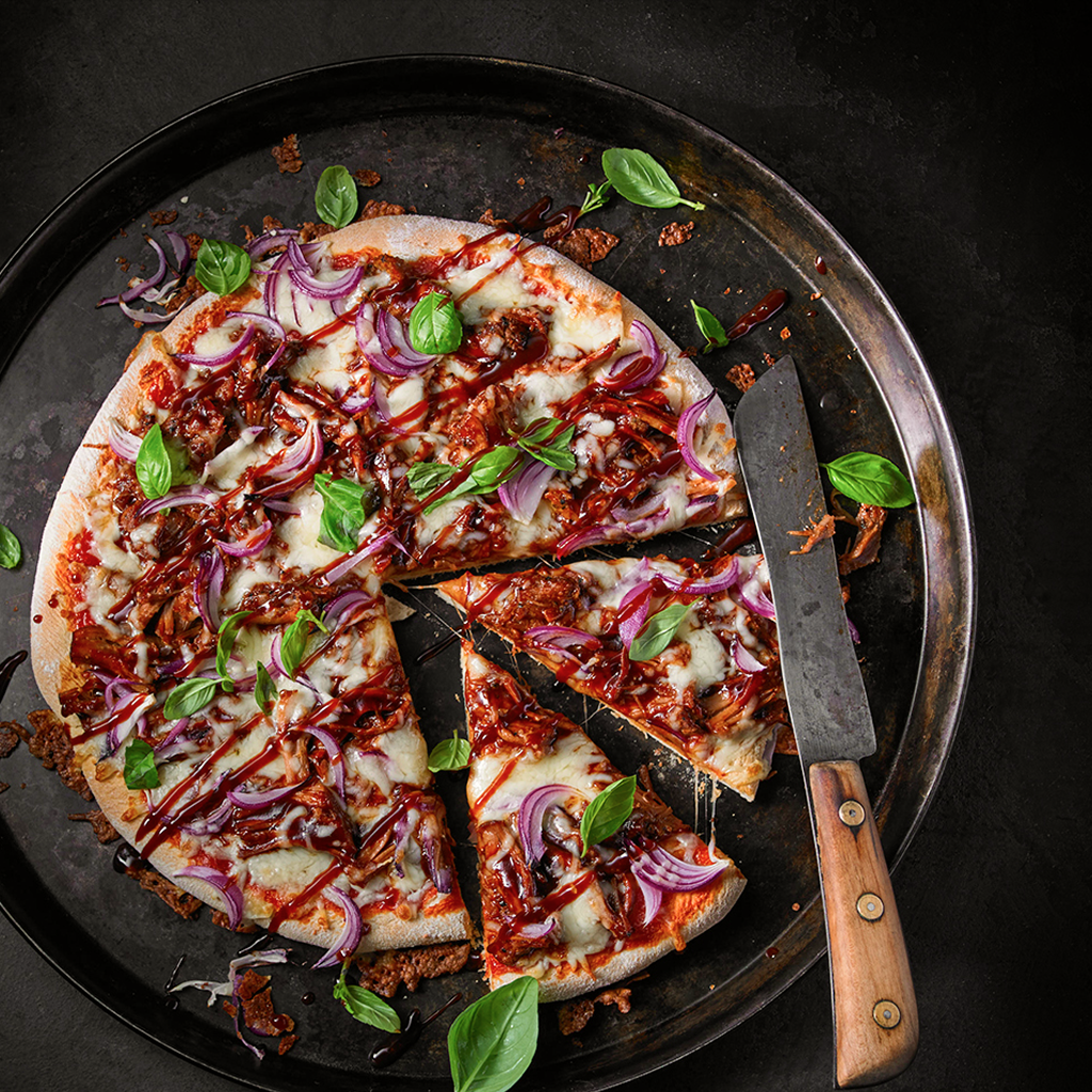 Frisch gebackene Pizza Special Pulled Pork BBQ mit knusprigem Boden, saftigem Pulled Pork, würziger BBQ-Sauce, geschmolzenem Käse und herzhaften Toppings auf einem Brett serviert.
